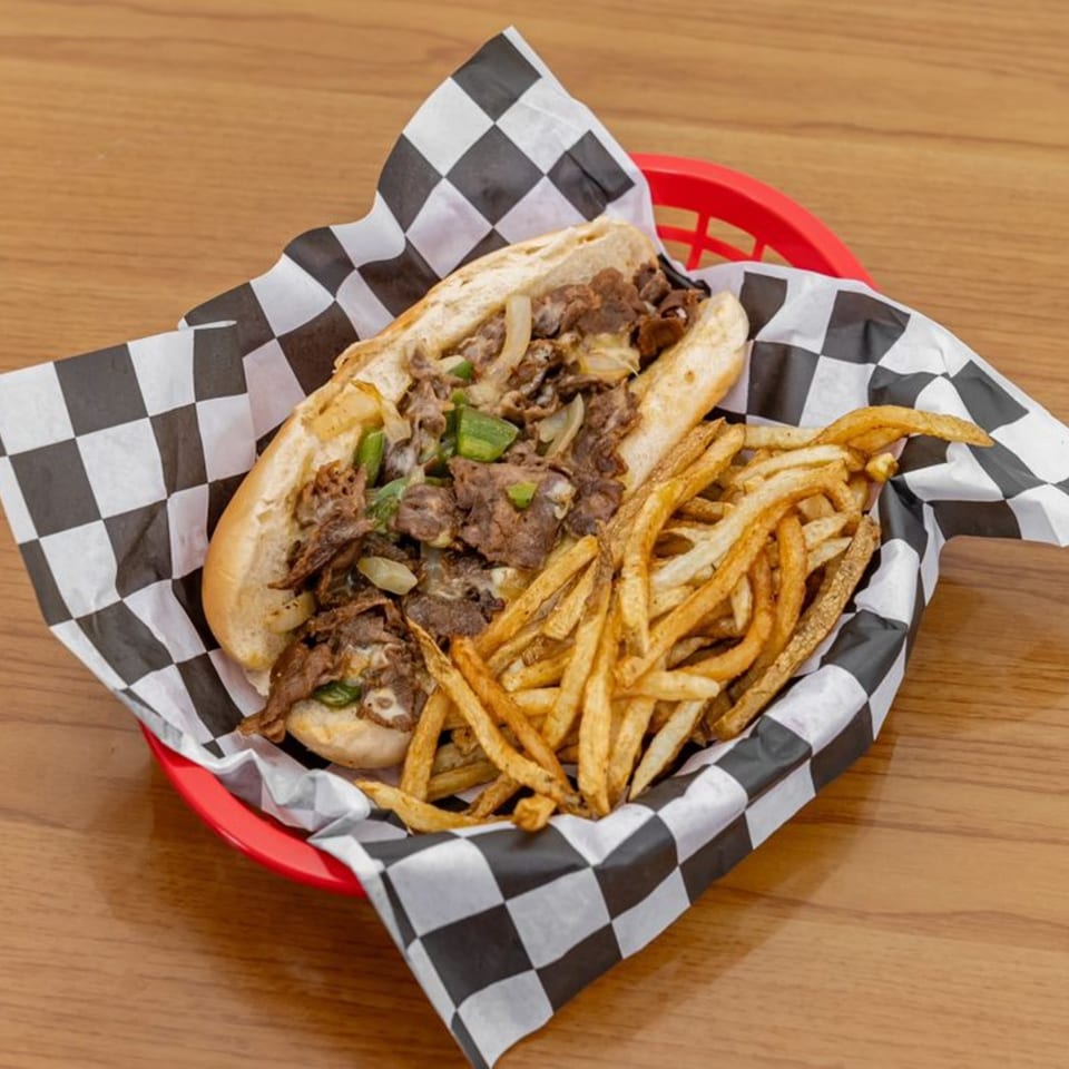 A Hyde Out Grill cheesesteak with onions and peppers, served with fries in a red basket.