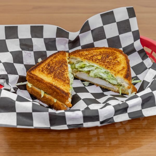 A grilled chicken sandwich, cut in half, with lettuce and sauce, served in a red basket with checkered paper.