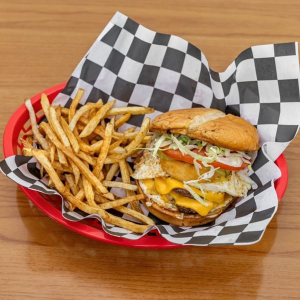 A Hyde Out Grill burger with cheese, fried egg, lettuce, tomato, and fries in a red basket.