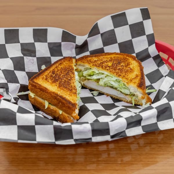 Grilled chicken sandwich with shredded lettuce, cut in half, served in a red basket with checkered paper.