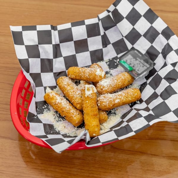 A red basket filled with golden-brown mozzarella sticks, sprinkled with parmesan cheese, on checkered paper.