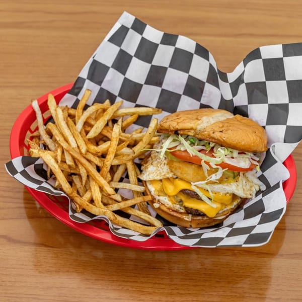 A double cheeseburger with a fried egg, lettuce, and tomato, served with fries in a red basket.