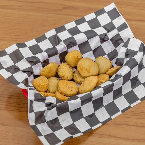A red basket filled with golden-brown fried pickles, lined with black and white checkered paper.