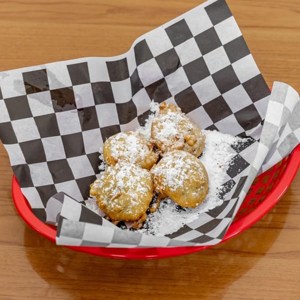 Four golden-brown fried dough balls, dusted with powdered sugar, in a red basket with checkered paper.