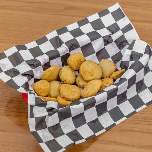 A red basket filled with golden-brown fried pickles, lined with black and white checkered paper.
